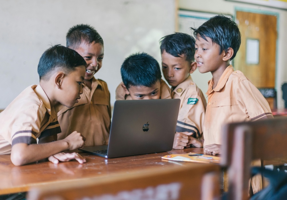Children gathering around a laptop, looking at an eCard