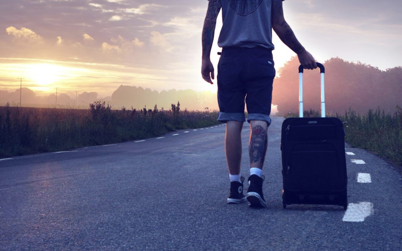 person walking away on road with suitcase