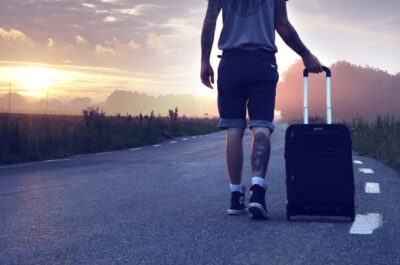person walking away on road with suitcase